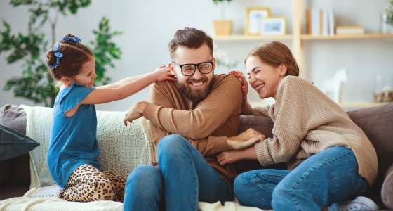 Little girl tickling her father on a sofa with her mother